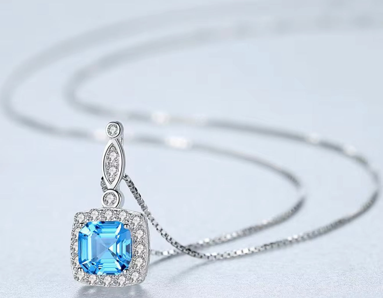Silver necklace with a blue gemstone pendant on a light gray background