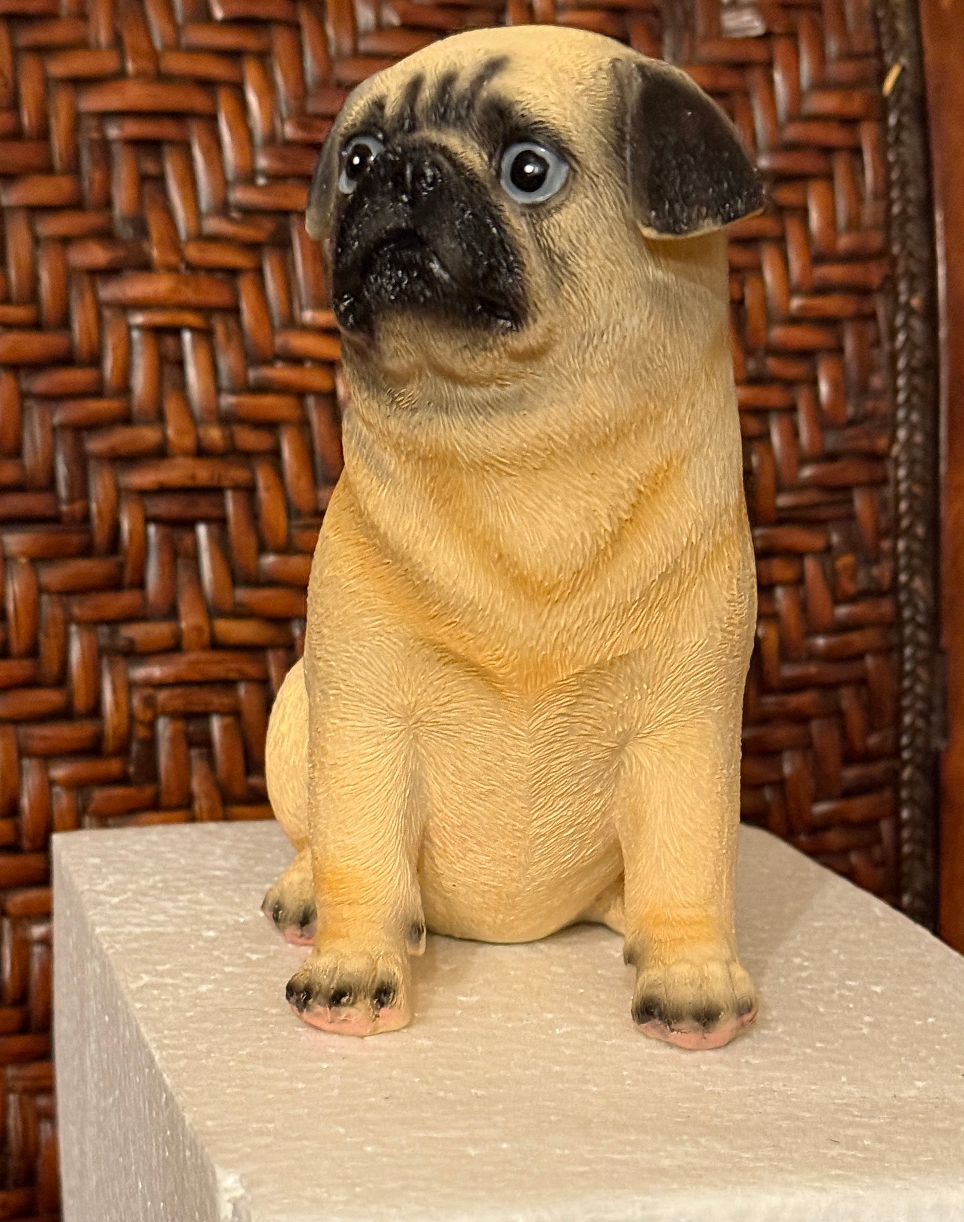 Miniature pug dog toy sitting on a textured surface with a woven brown background